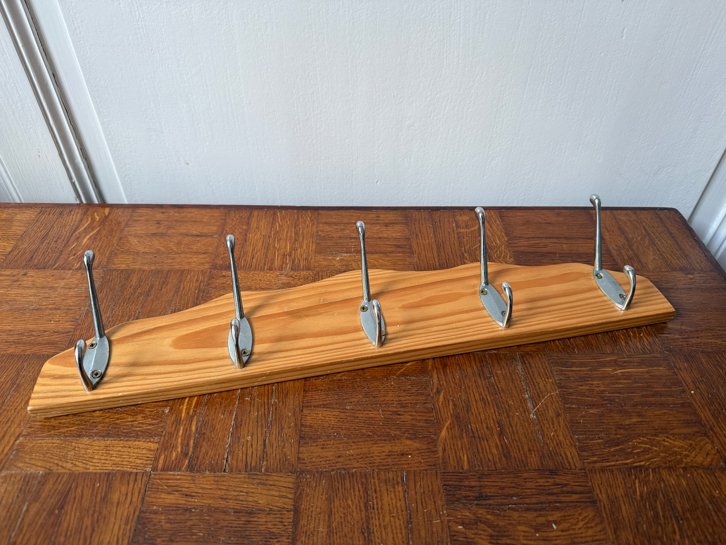 Wood and metal wall coat rack by Razzia with hooks and storage space, mounted on a modern living room wall.