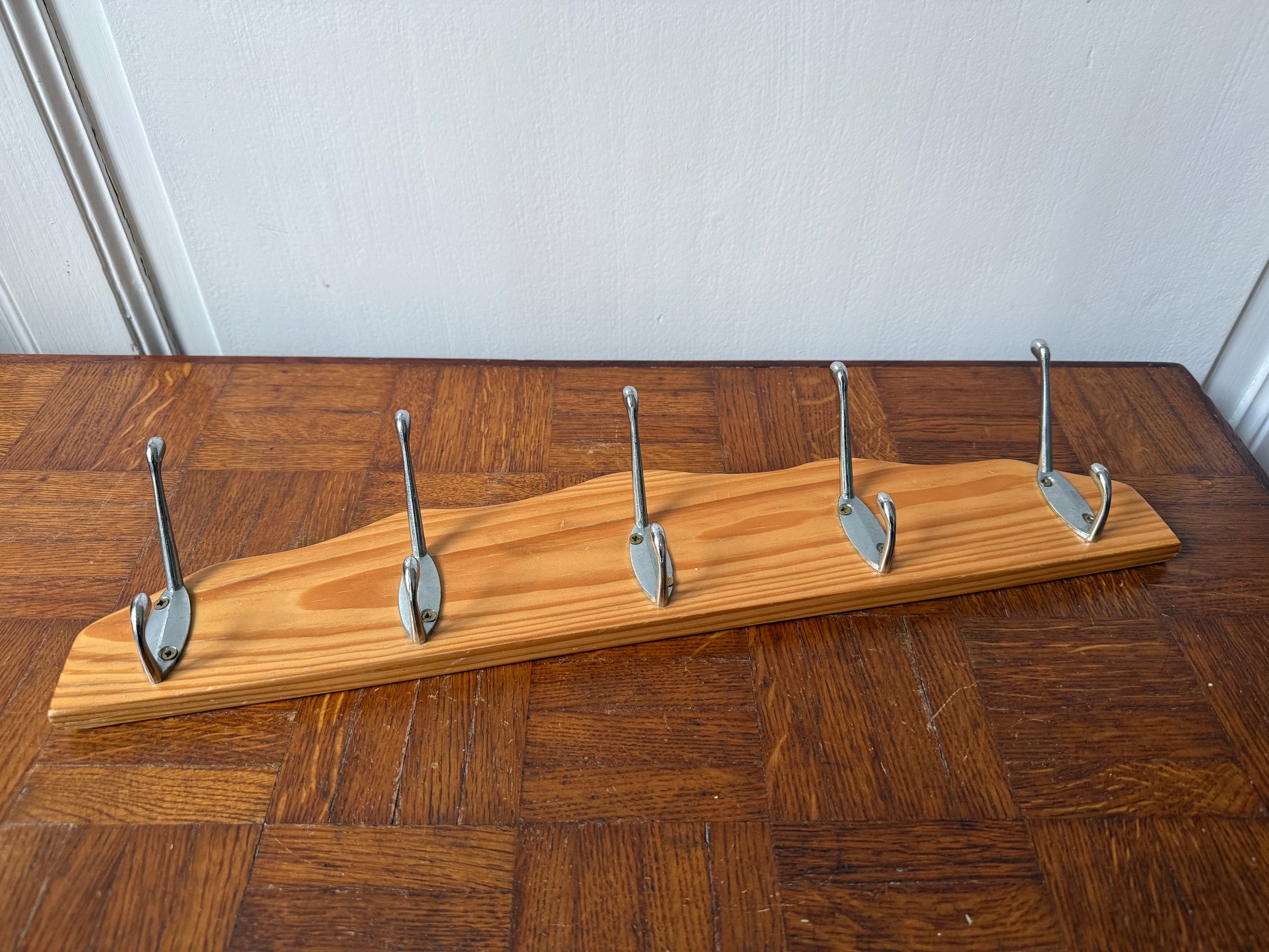 Wood and metal wall coat rack by Razzia with hooks and storage space, mounted on a modern living room wall.