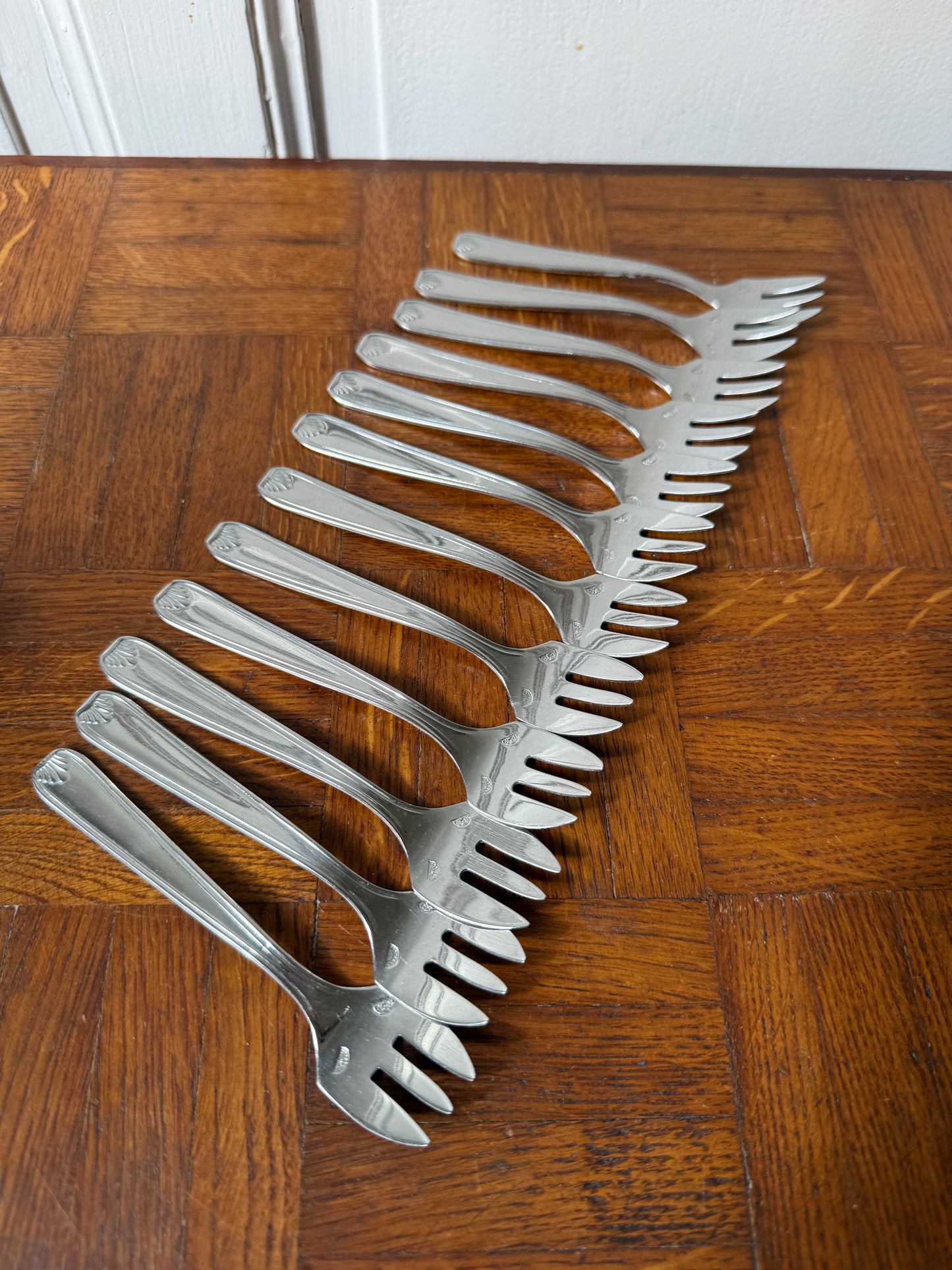 Douze fourchettes à dessert en argent Razzia disposées sur une table, élégantes et brillantes, pour une présentation raffinée.