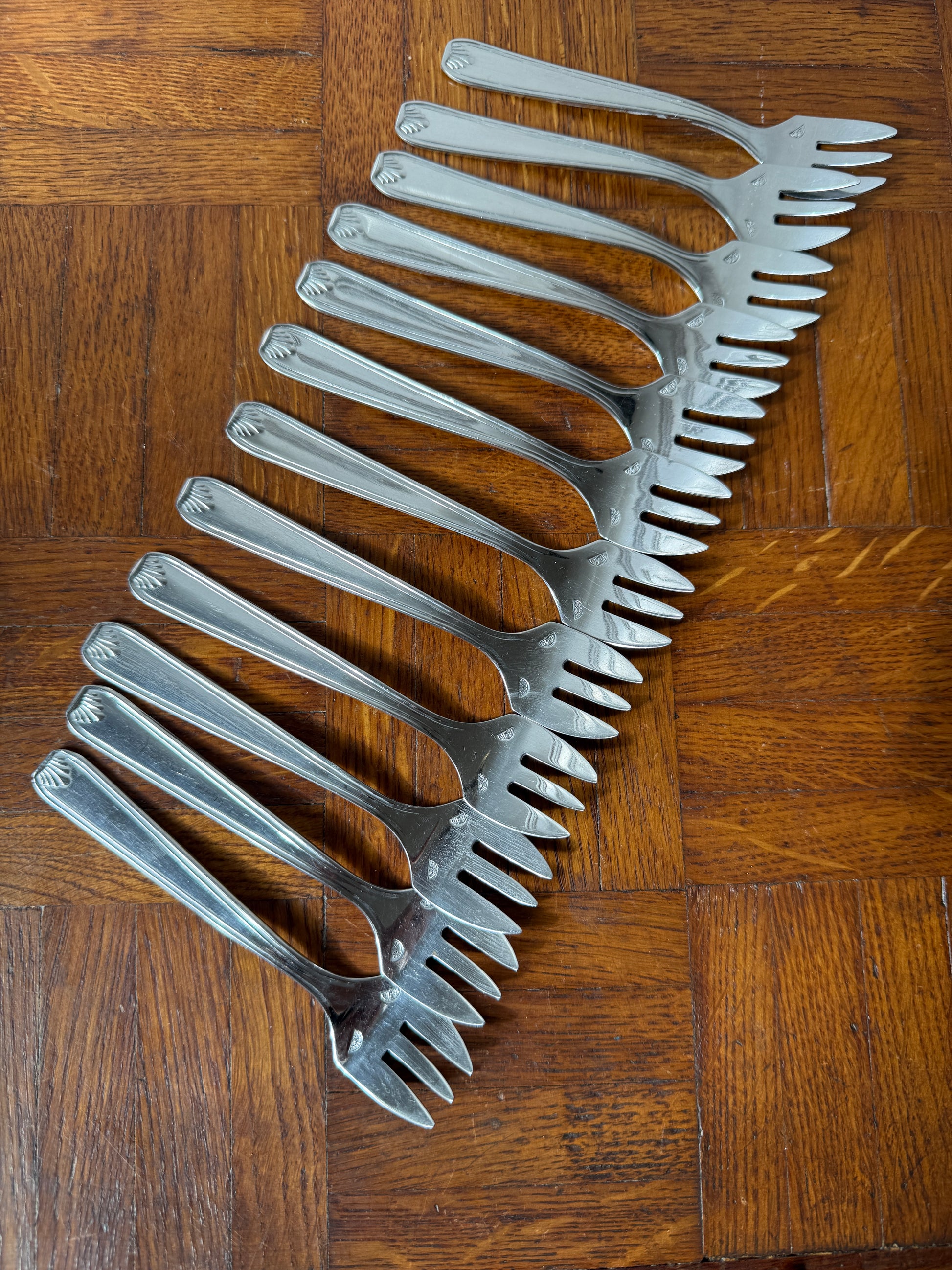 Set de 12 fourchettes à dessert en argent Razzia, élégantes et brillantes, disposées sur un fond blanc.