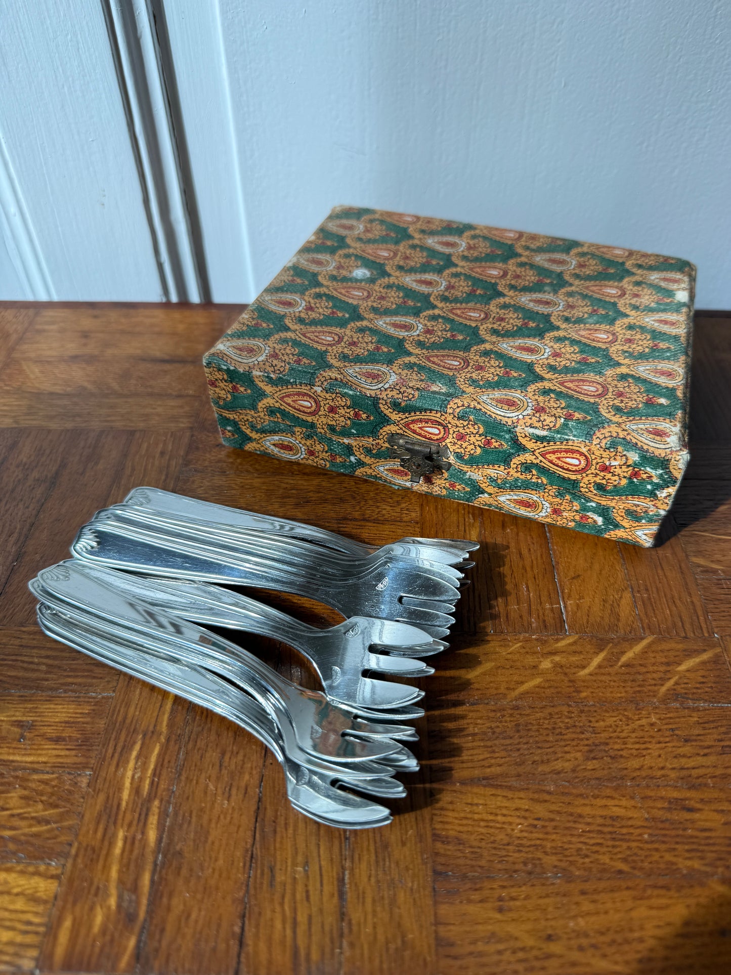Douze fourchettes à dessert en argent Razzia, élégantes et brillantes, disposées sur une table en bois.