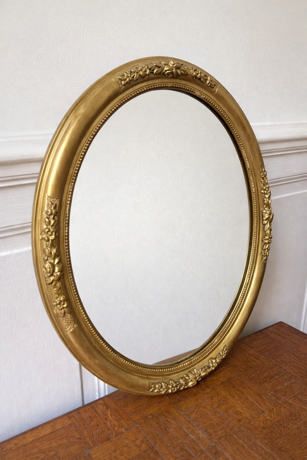 Miroir ovale doré de style victorien posé sur un parquet, design élégant et classique de la marque Razzia.