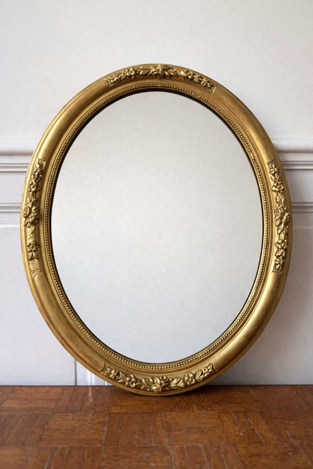 Miroir doré ovale de style victorien posé sur un parquet, design élégant et orné, de la marque Razzia.
